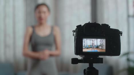 close up de un monitor de cámara grabando entrenadora asiática mujer en ropa deportiva agitando la mano y hablando mientras enseña ejercicios en casa