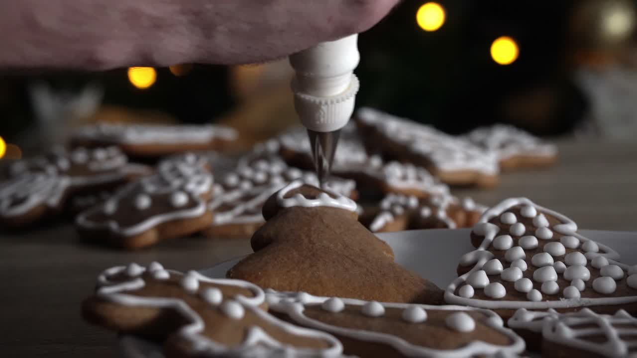 Male chef decorating gingerbread tree with white sugar icing with Christmas tree in the background