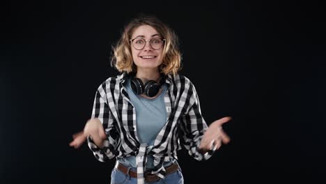 mujer excitada con peinado rizado, ríe felizmente, expresa emociones sinceras, sorprendida por buenas noticias. mujer joven feliz en camisa a cuadros y vaqueros gestando, súper sorprendida por el fondo negro