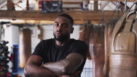 Portrait-Of-Male-Boxer-In-Gym-Standing-By-Old-Fashioned-Leather-Punch-Bag