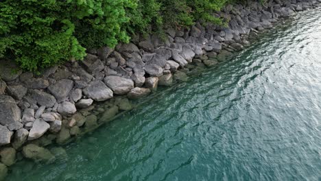 Fascinante-Calma-Relajante-Escena-Pacífica-De-Las-Aguas-Onduladas-Del-Lago-Que-Llegan-A-Las-Rocas-En-La-Orilla