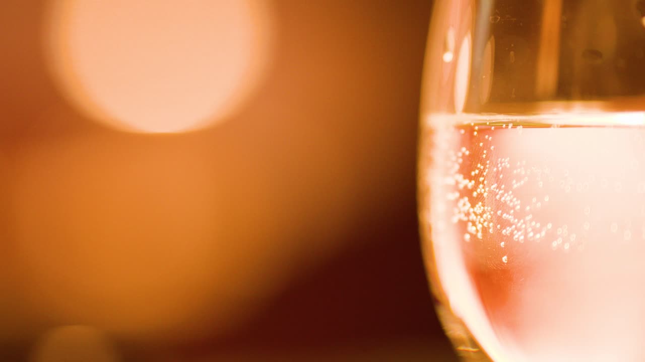Sparkling water bubbles rise in glass, warm bokeh lighting, elegant bar atmosphere, macro close-up