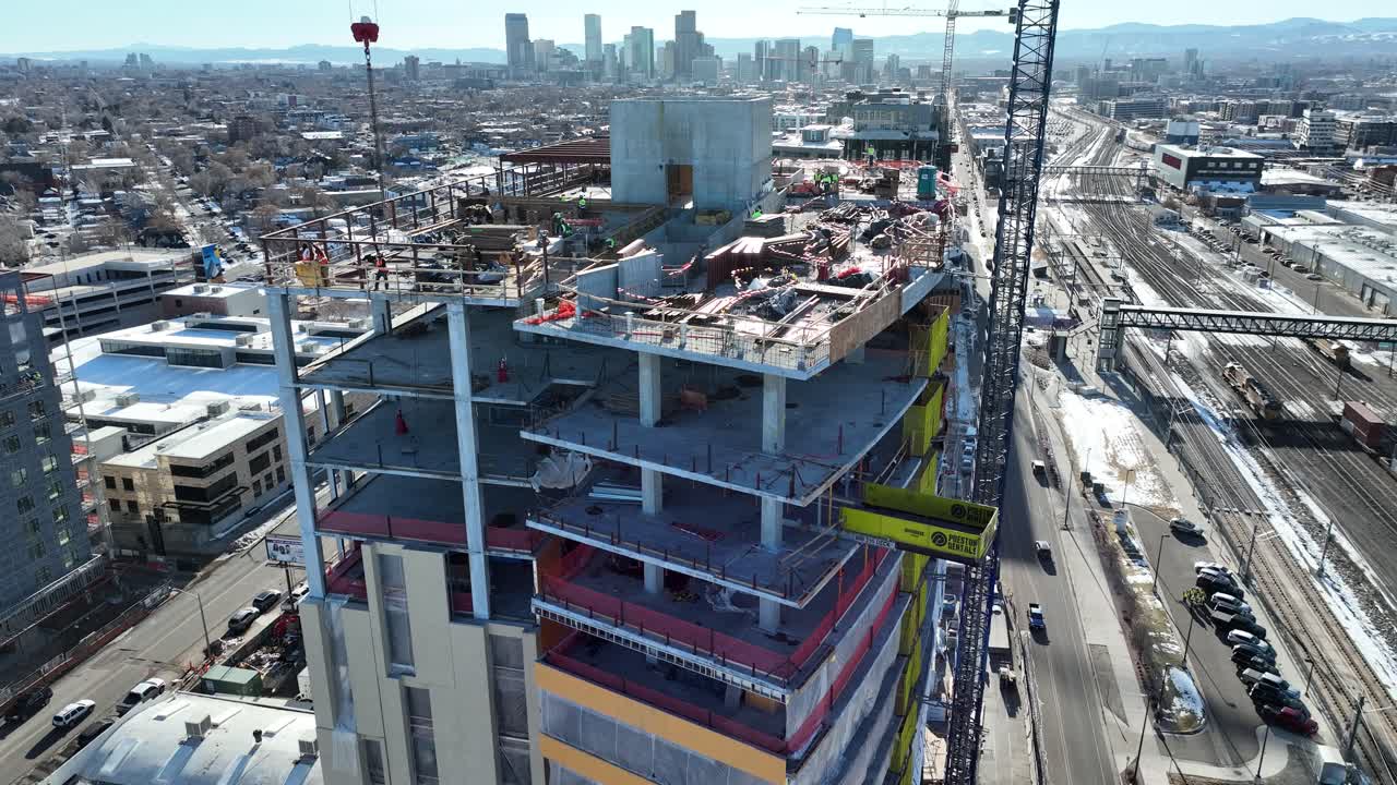 drone volando y revelando lentamente edificios de varios pisos en construcción con trabajadores trabajando en el techo con vista al centro de la ciudad de denver, vista a la calle y vías férreas, colorado