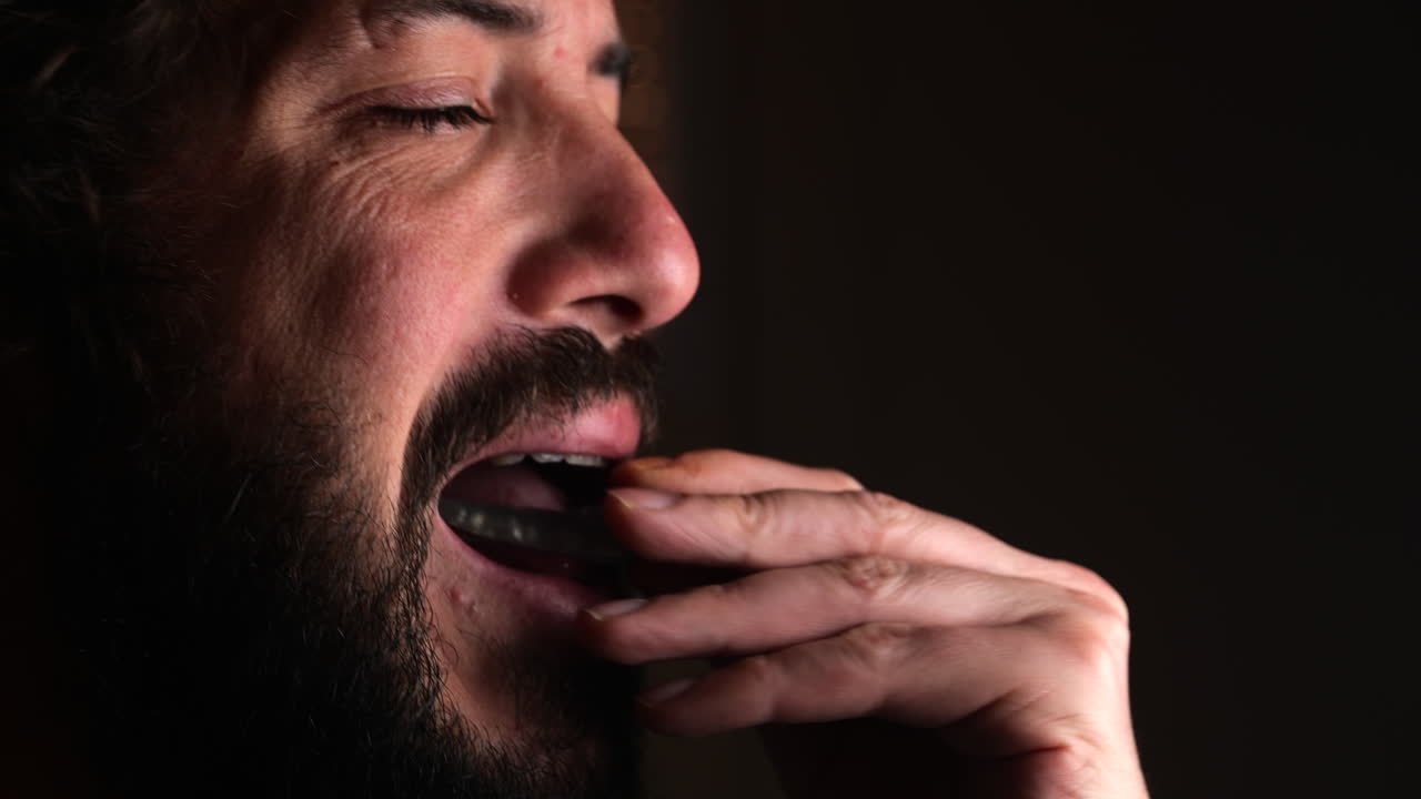 Close-up shot of Bearded man putting on teeth protector ferula splint, dark background