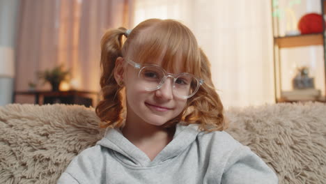 young teenager girl putting on glasses with a focused expression indoors at home sitting on sofa