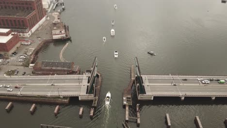 Toma-Aérea-De-Una-Línea-De-Barcos-Que-Navegan-Bajo-Un-Puente-Levadizo-En-El-Río-Místico