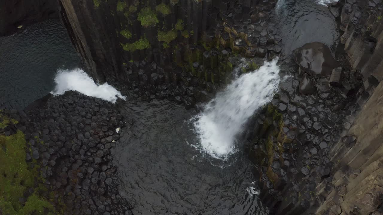 vista aérea de arriba hacia abajo de la cascada de litlanesfoss que cae en el lago islandés con columnas de basalto y rocas