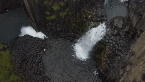 Antena-Arriba-Hacia-Abajo-De-La-Cascada-De-Litlanesfoss-Que-Cae-Al-Lago-Islandés-Con-Columnas-De-Basalto-Y-Rocas