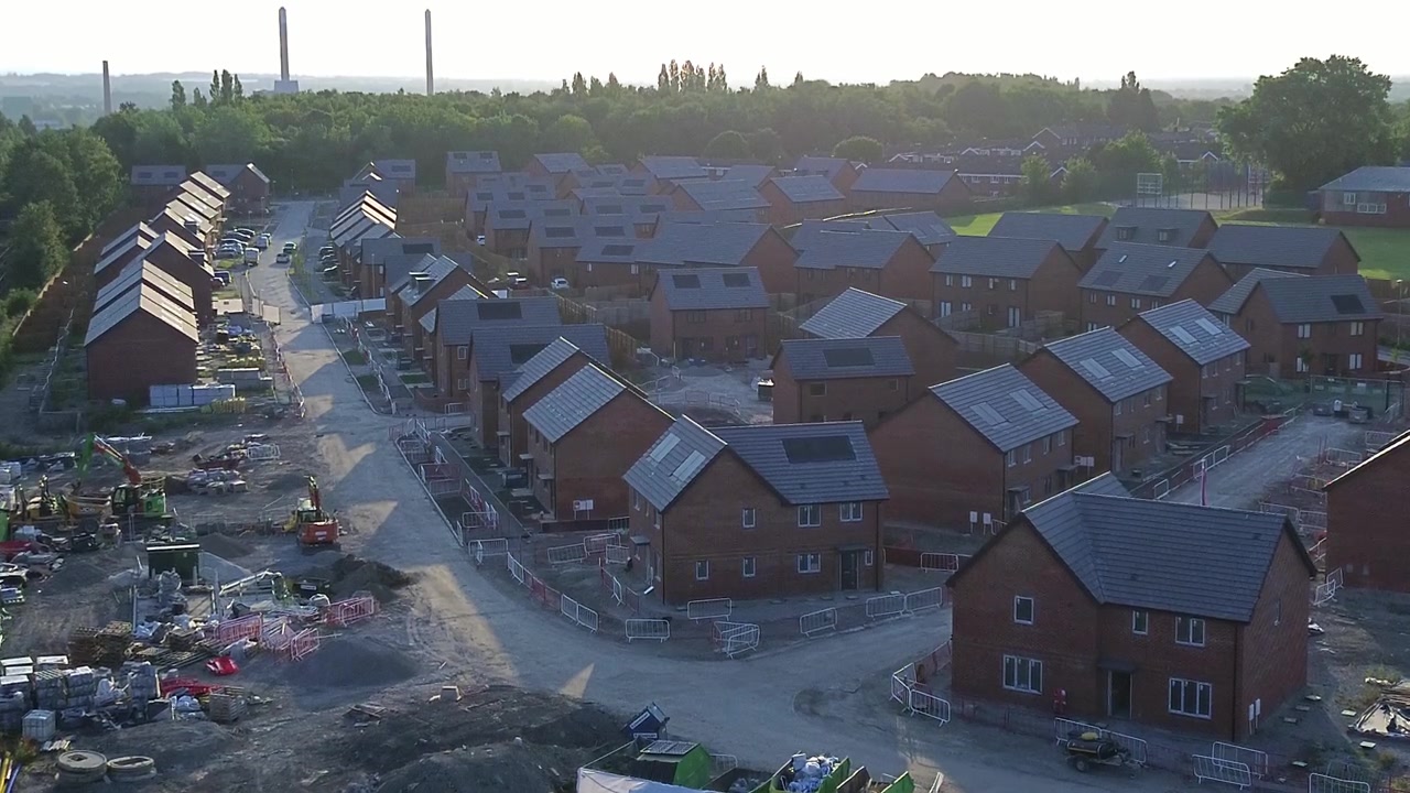 Unfinished new home framework construction site aerial view towards development estate rooftops