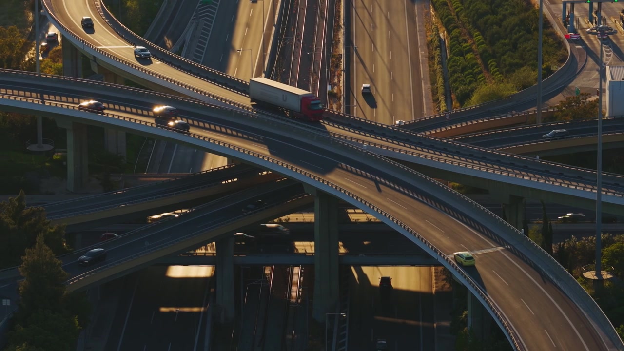 Golden hour sunlight illuminating a complex, multi-level highway interchange with cars, trucks, and buses driving along curved overpasses, illustrating modern transportation infrastructure