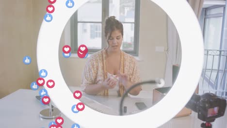 animation of love and like icons over female vlogger with ring light recording vlog at home