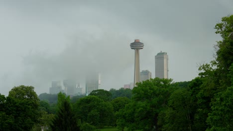 Foto-Pintoresca-De-La-Torre-Skylon-En-Las-Cataratas-Del-Niágara,-Ontario,-Con-Niebla-Elevándose-Desde-Las-Cataratas,-Enmarcada-Por-Un-Dosel-De-árboles-Verdes-Y-Frondosos.