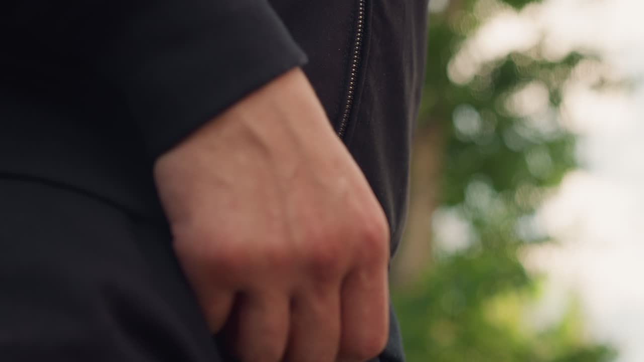 손으로 지퍼를 잠그는 모습이에요. 백인 남성이 야외 초목을 배경으로 조심스럽게 지퍼를 올리고 있어요. 남성의 손이 미묘한 야외 녹색 잎 배경을 뒤로하고 지퍼를 잠그는 모습이 자세히 촬영되었어요.