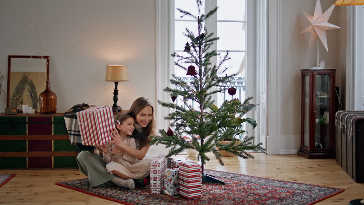 una linda caja de regalos de la familia cerca del árbol de navidad. mujer abrazando a la niña en un hogar acogedor