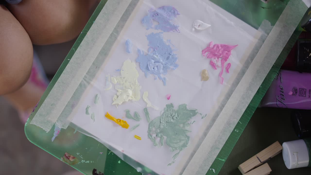 A person's hand mixes colorful paints on a palette with a paintbrush
