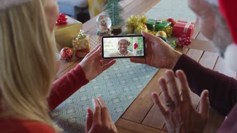 Kaukasisches-Paar-Mit-Weihnachtsmützen-Nutzt-Smartphone-Für-Weihnachtsvideoanruf-Mit-Freund-Auf-Dem-Bildschirm