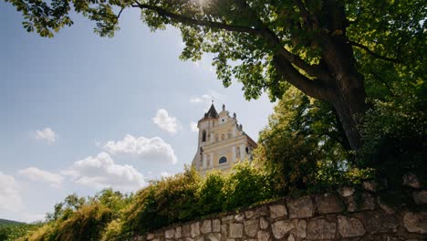 catholic church falkenstein behind a stone wall tilting up to a big tree with sun shining through branches in austria