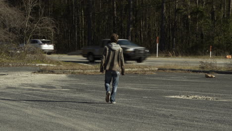 young man walks away towards busy rural road outside, sunny day, wide