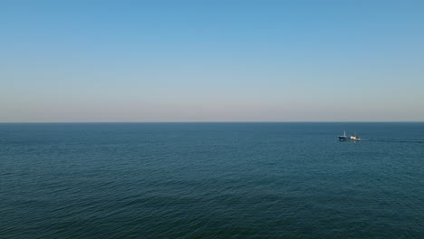 A-fishing-boat-sails-on-the-calm-Baltic-Sea,-the-rolling-sea-and-clear-sky-on-the-horizon,-Hel-Poland