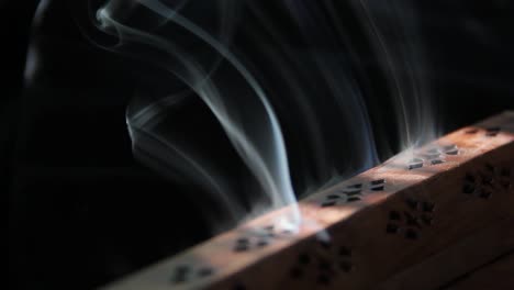 incense smoke curls out of a wooden incense burner