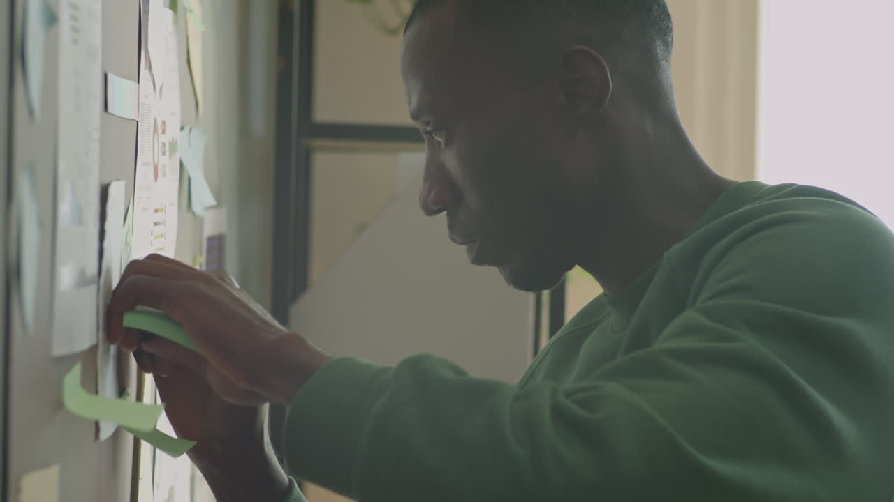 Black Man Writing on Sticky Notes Attached to Office Wall
