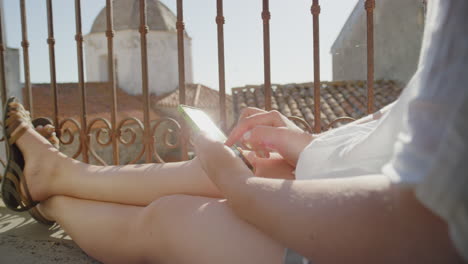 young woman using smartphone browsing online sending text messages enjoying sharing summer vacation experience relaxing on balcony in rustic villa close up