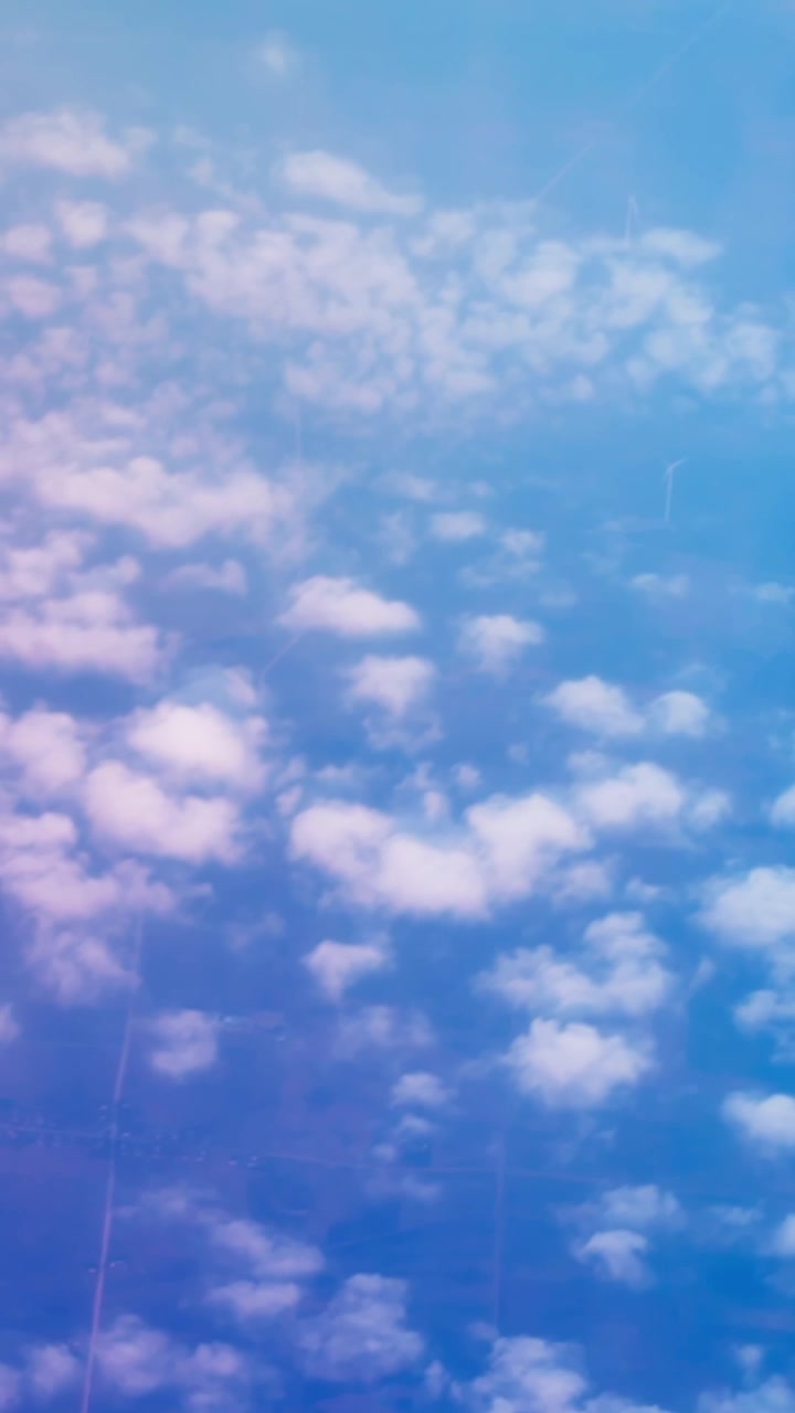 Vertical aerial view of scattered white clouds over a soft blue sky, creating a dreamy high-altitude atmosphere with gentle light and calm minimal scenery.