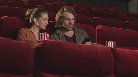 happy couple sitting in movie theater and looking something funny on the mobile phone