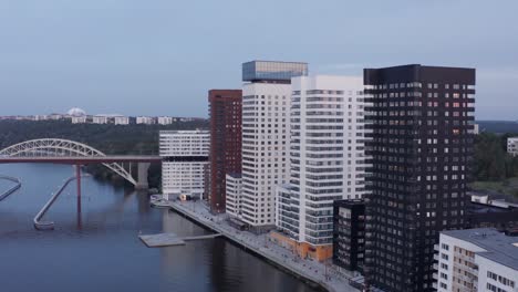 Drone-footage-of-high-rise-residential-buildings-with-modern-design-and-architecture-in-Årstadal,-Stockholm-with-train-passing-on-bridge