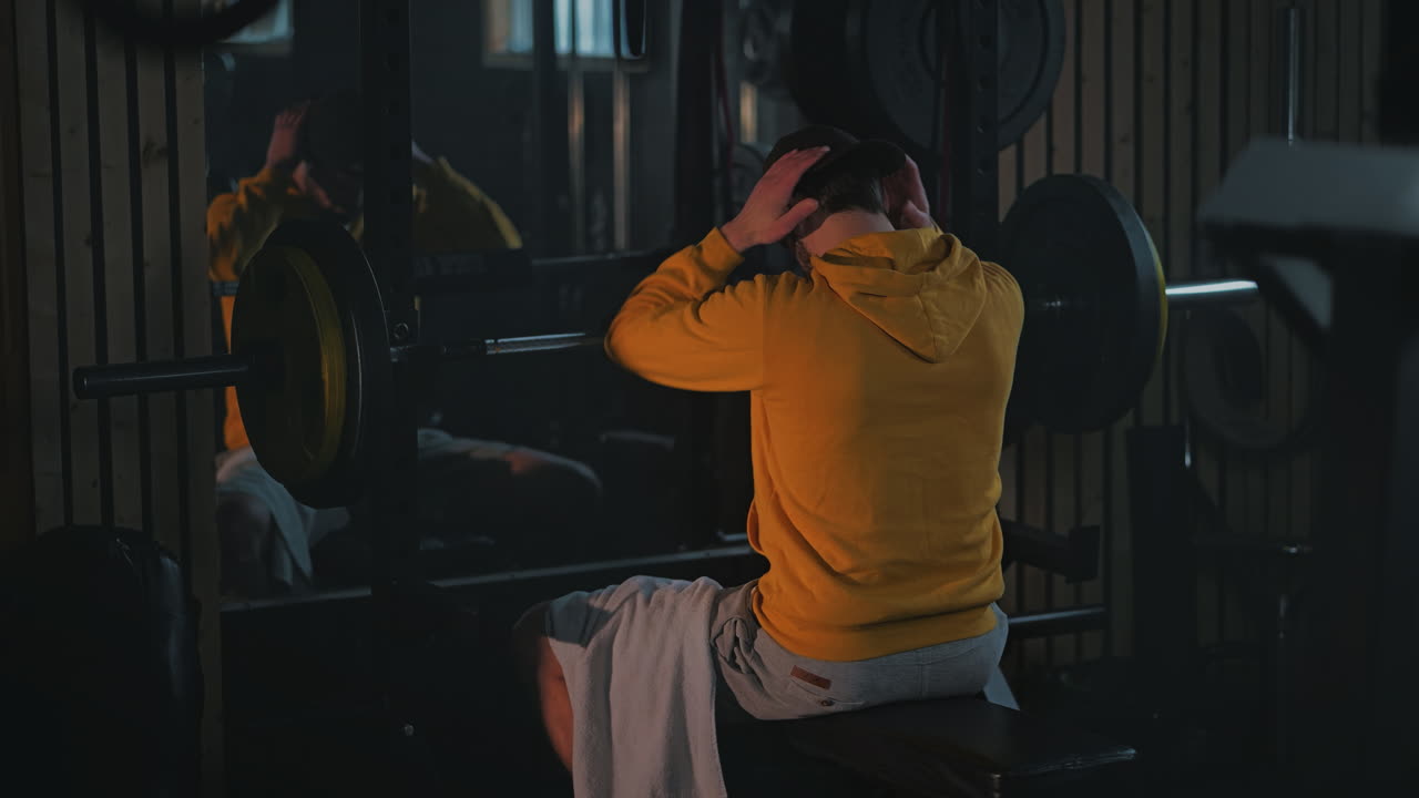 Man rests and wipes sweat between sets on gym weight training bench