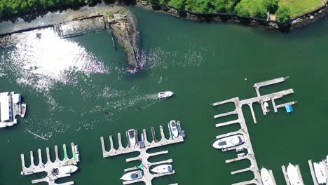 an aerial view over a dock on a sunny day. the drone camera looks straight down and rotates clockwise over a boat going out and one coming in. the water is calm and green as the sun reflects on it