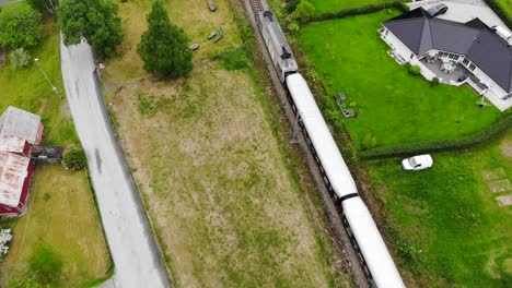 Aerial:-Flåm-train-going-through-a-valley-among-green-meadows-and-some-houses