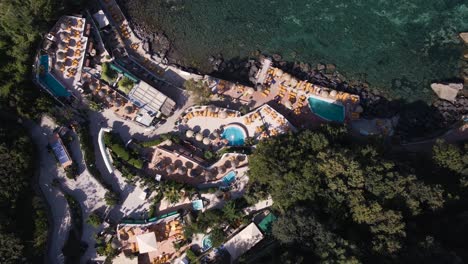 birds eye view of a resort spa with heated pools and plenty of umbrellas beside the mediterranean sea during a hot summers day located on the tropical island of ischia off the coast of naples in italy