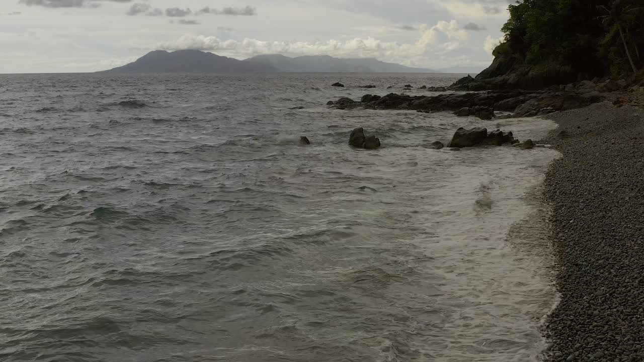 Onde oceaniche che si infrangono spargendo schiuma bianca sulla spiaggia di ciottoli di Looc, perfetta serenità