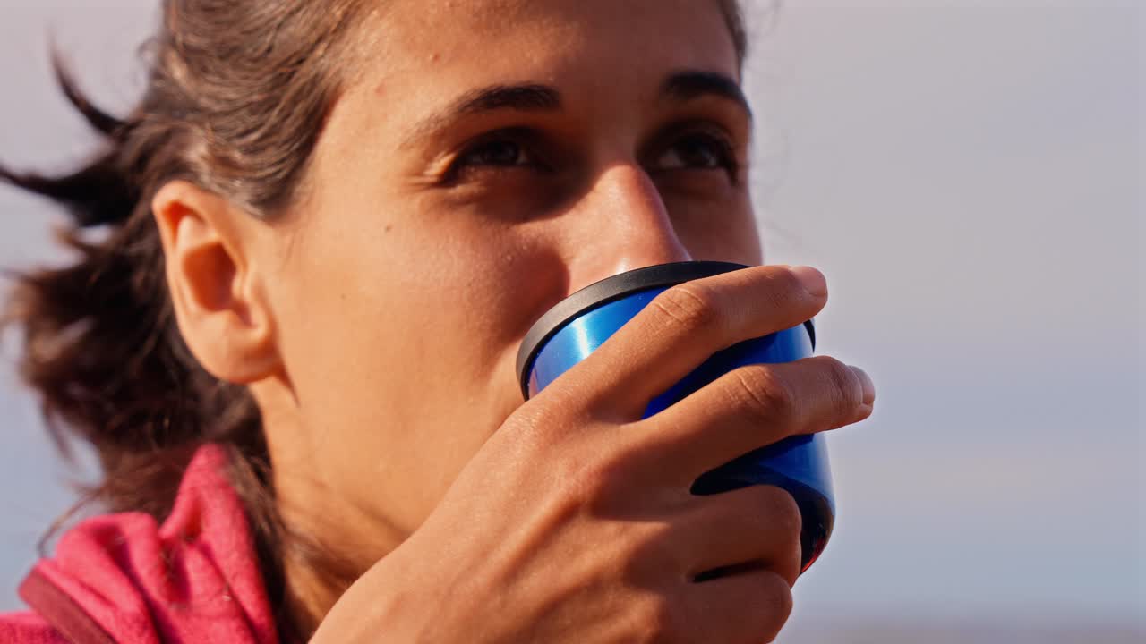 A person is holding a blue cup and appears to be enjoying a warm drink outdoors, with a relaxed, contemplative mood.