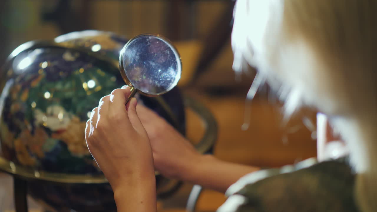 손에 돋보기를 가진 여자는 큰 지구 다시 보기를 검사합니다.