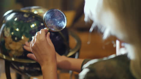 woman with magnifying glass in hand examines big globe back view