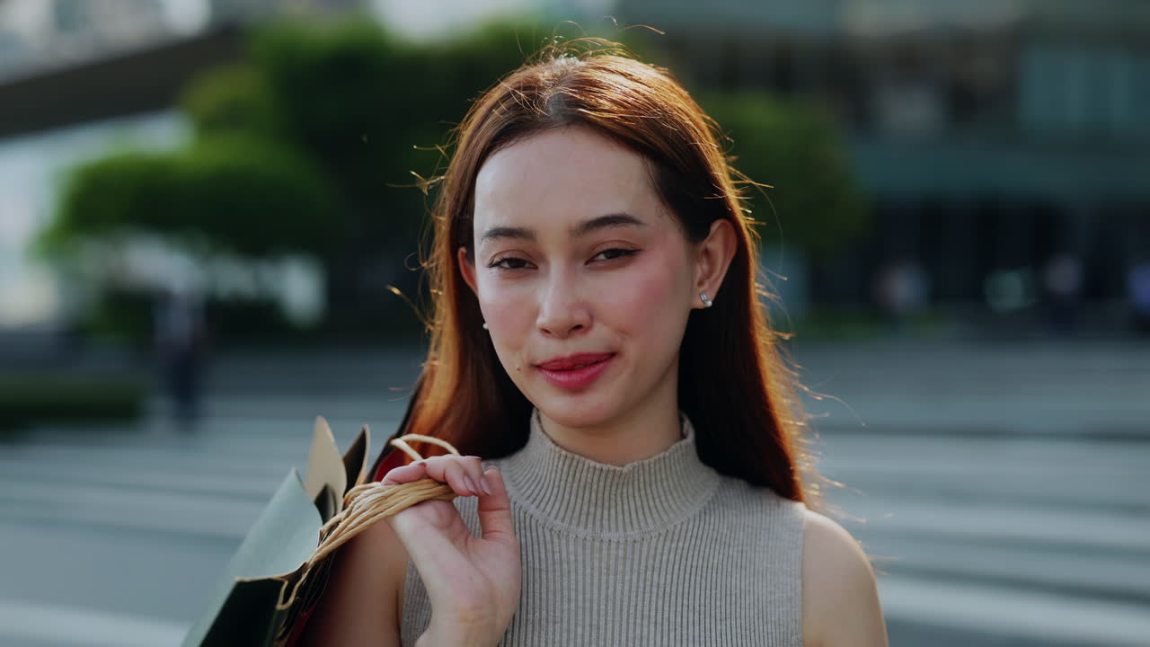 開心的年輕亞洲女士在戶外手持購物袋面帶笑容。