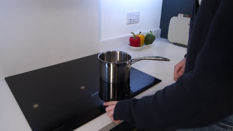 Female-model-putting-a-pan-of-water-on-a-induction-cooker-top-and-turning-it-on,-in-a-kitchen