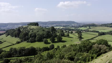 AERIAL---Couple-walk-their-dog-on-a-hill,-Uley,-Cotswolds,-England,-forward-reveal