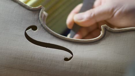 macro-close-up-of-artisan-luthier-maker-work-on-new-classic-handmade-raw-violin-smooth-edge-in-waist-and-purfling-rasp-in-workbench-of-workshop-in-Cremona-Italy-4k-video