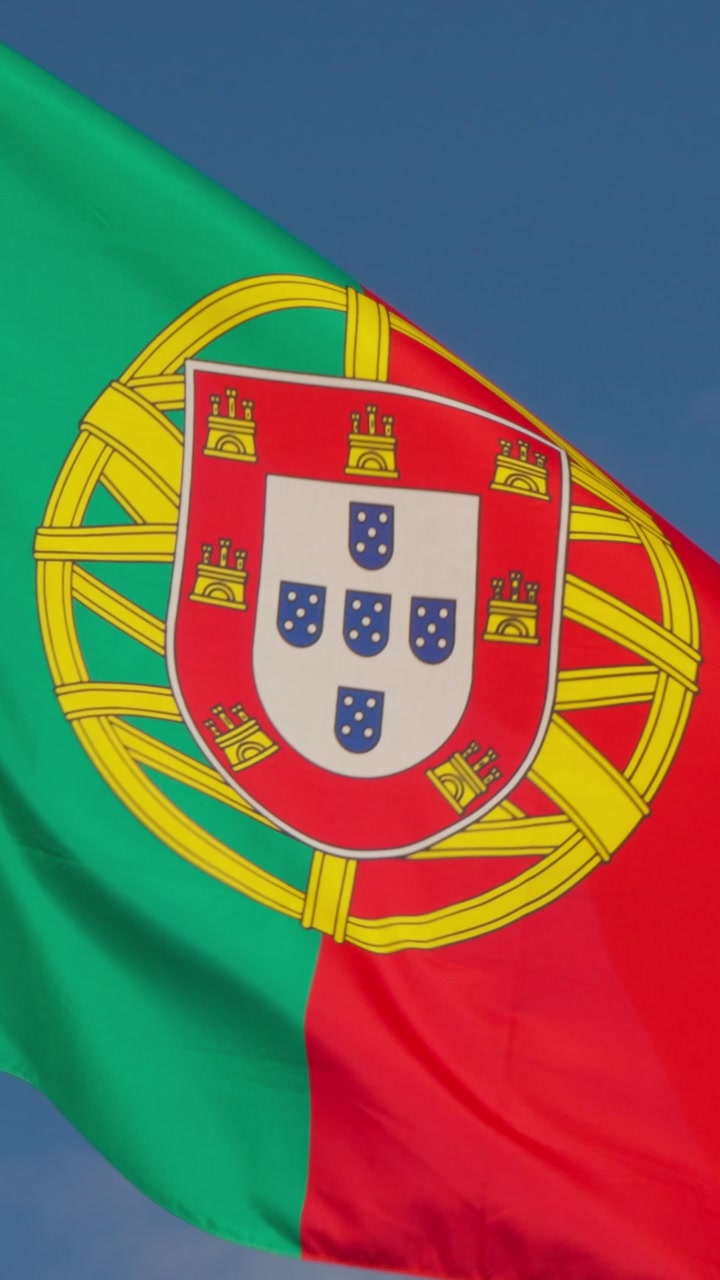 National flag of Portugal waves gracefully against a clear bright blue sky. This vibrant symbol represents Portuguese identity, history, and culture, perfect for themes of travel, international eve...