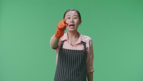wütende asiatische weibliche haushälterin mit schürze, die auf die kamera zeigt und schreit, während sie im studio mit grünem bildschirm steht