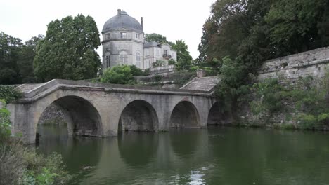 Agua-Verde-Y-árboles-En-El-Parque-Circundante-En-Chateauneauf-Sur-Loire,-Con-Un-Puente-Arqueado-De-Piedra-En-Un-Día-Nublado