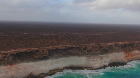 aerial tracking shot of white camper van on empty road along rugged coastline in south australia