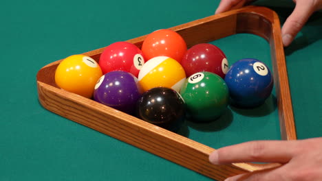 el hombre rueda el estante de diamantes de la piscina de 9 bolas en el marco en el primer plano del lugar en una mesa con fieltro o tela verde y aprieta el estante con las manos antes de levantar el triángulo de madera