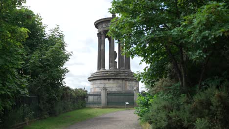 reveal behind trees of dugald steward monument in edinburgh scotland