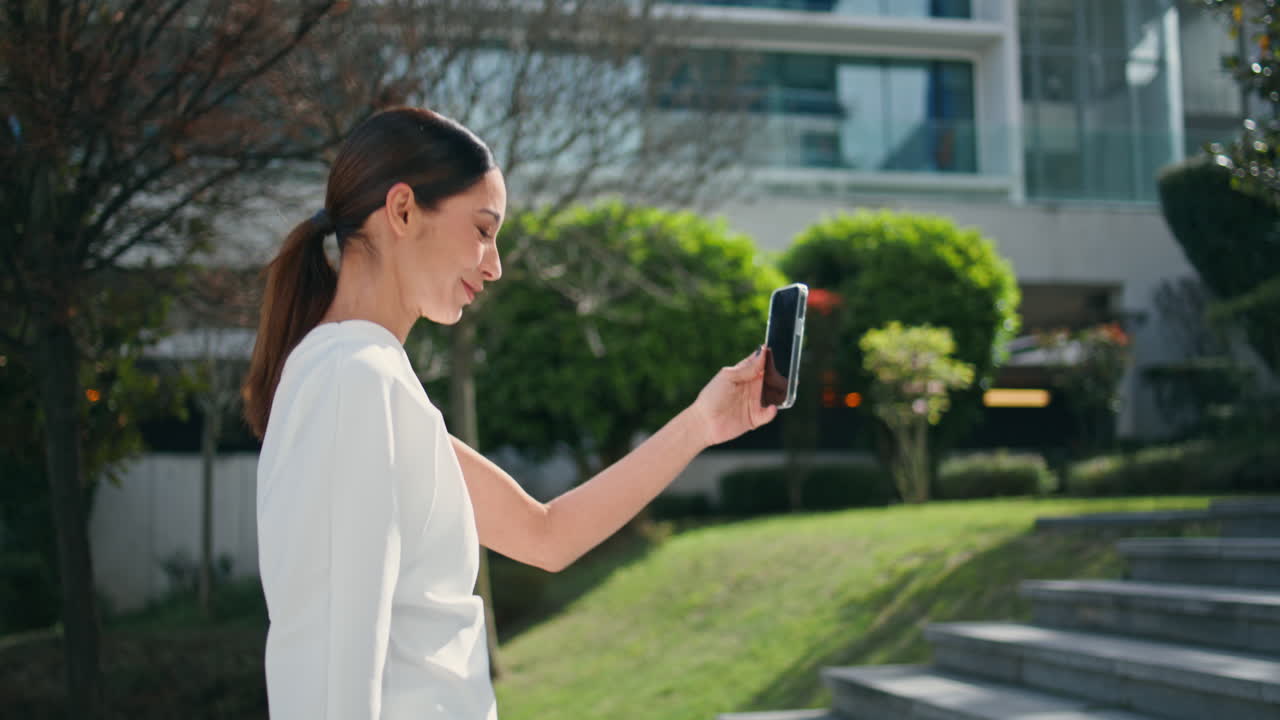 mujer de negocios sonriente video llamadas telefónicas caminando arriba calle soleada primer plano