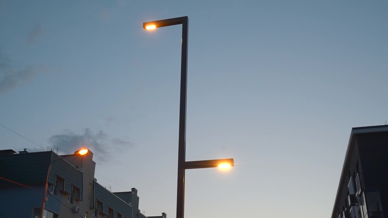 クリップ全体を通して、日光が夕暮れへと薄れていく中、高い街灯が都市の屋根の上に立っている。最初から最後まで、暖かな光がより際立っていく。