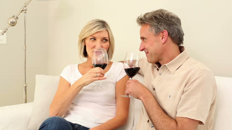 una pareja madura tomando vino rojo juntos en el sofá.